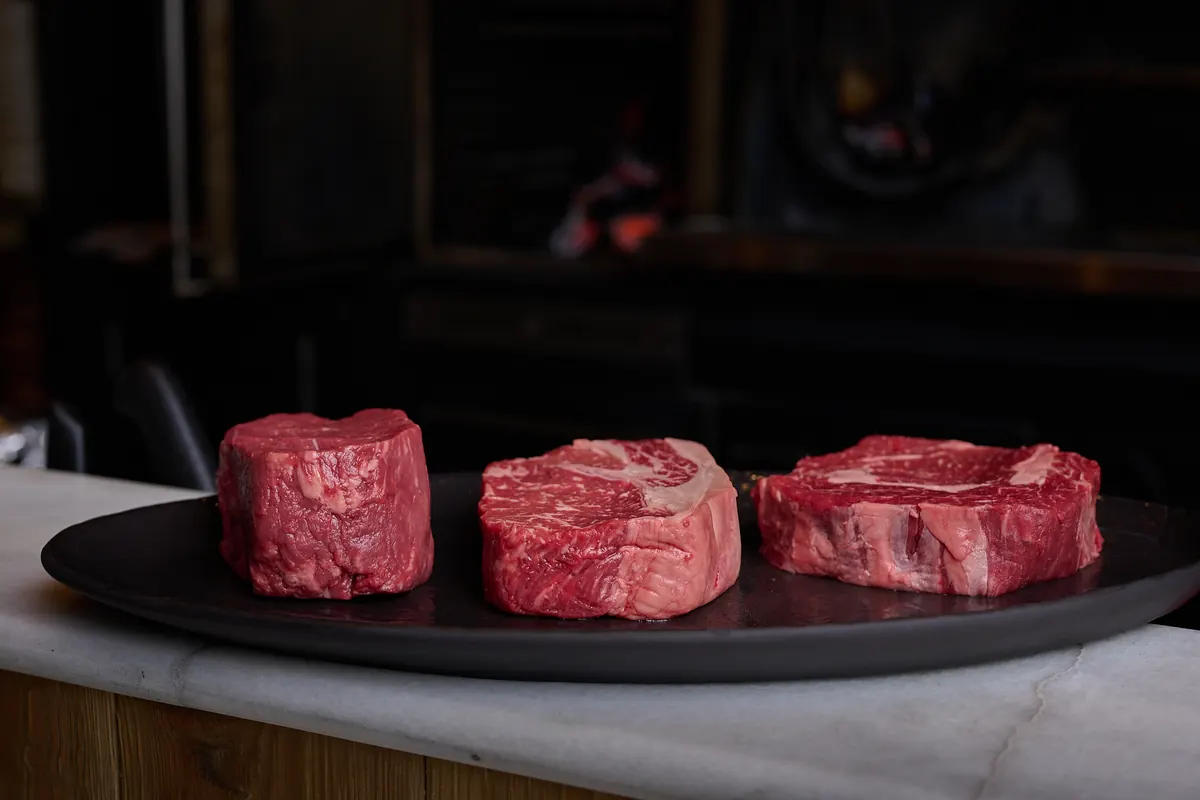 Tres cortes de carne cruda sobre una fuente negra, encima de una barra de mármol