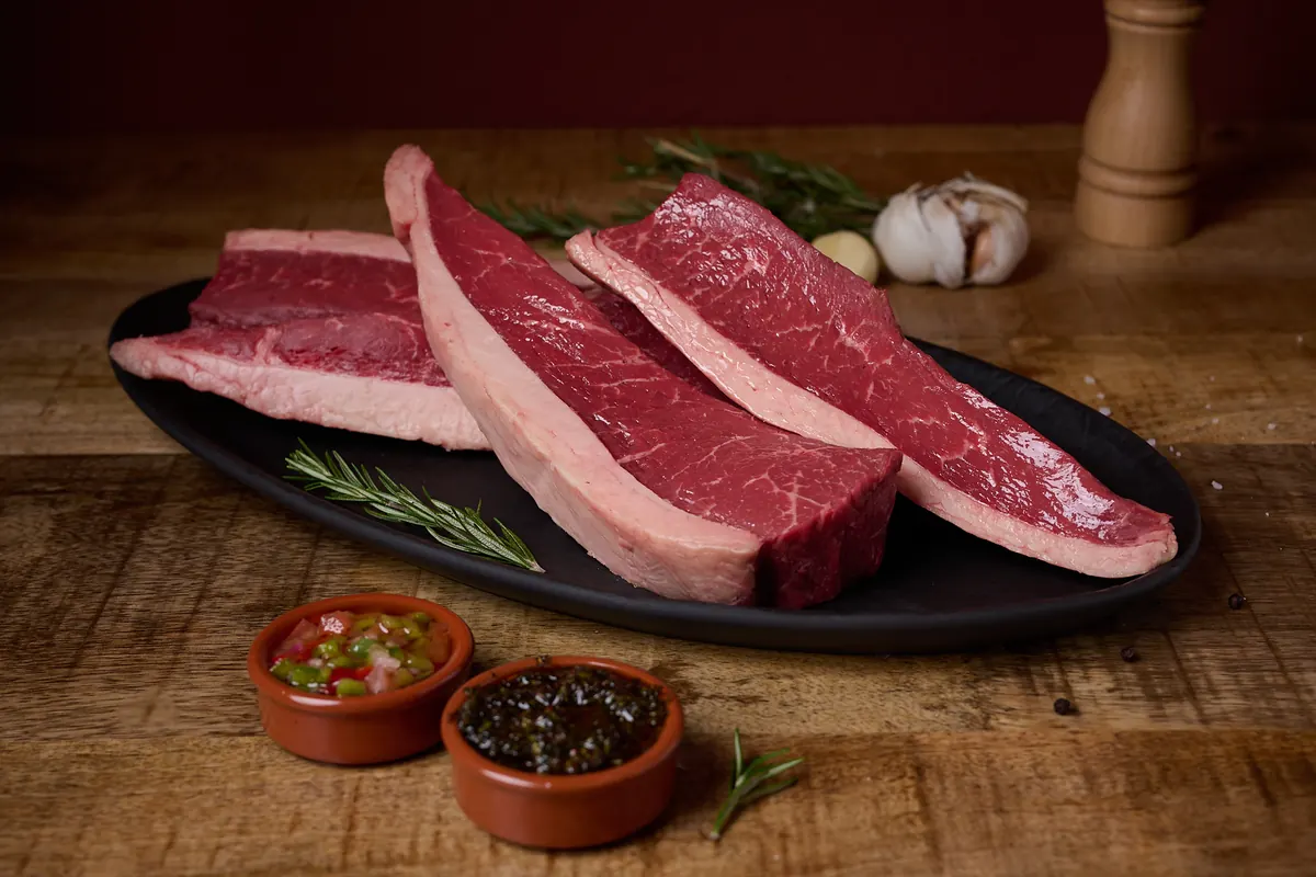 Cortes de carne cruda en una fuente negra, con dos salsas en cuencos de barro