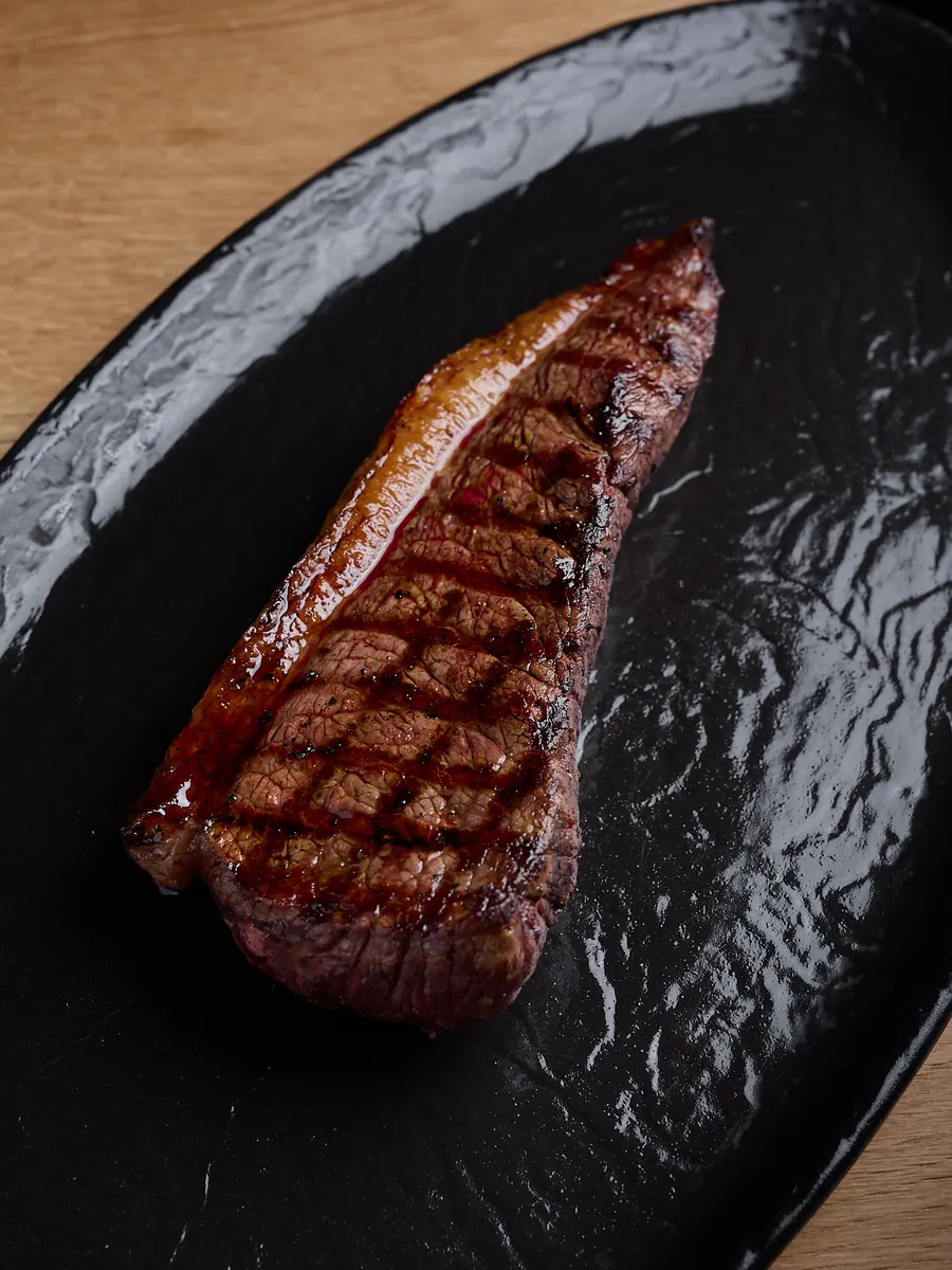 Una pieza de carne a la brasa con las marcas de la parrilla, sobre una fuente negra