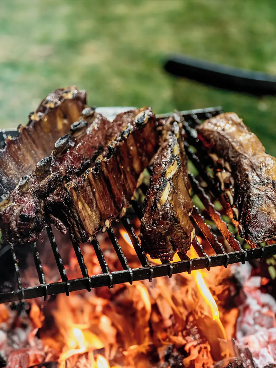 Un costillar y otros cortes de vacuno sobre una parrilla, con las brasas encendidas debajo