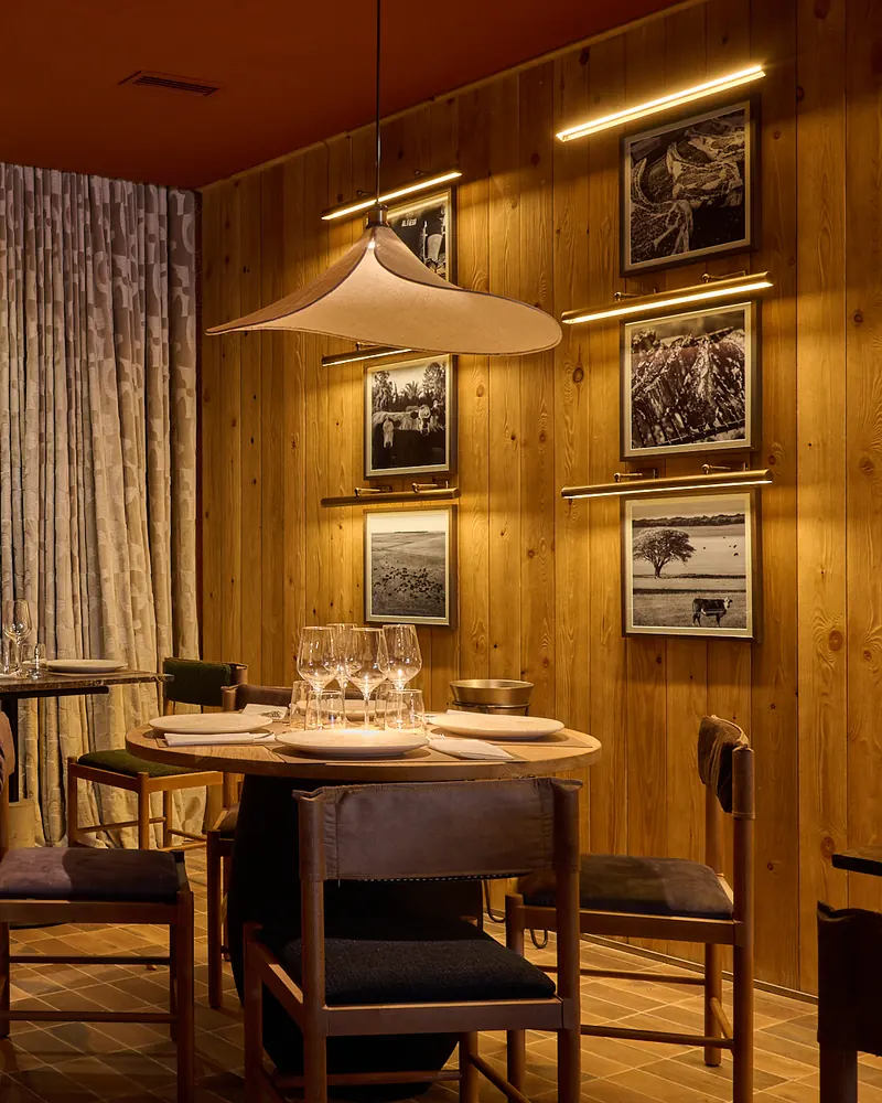 Una mesa redonda preparada junto a una pared de madera con fotos del campo en blanco y negro, en la sala de Al Fuego
